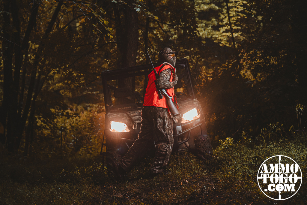 deer hunter A deer hunting walking through the woods in front of an ATV with its lights on