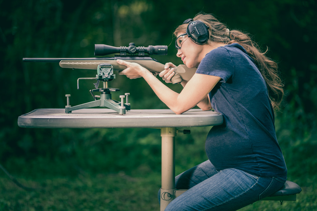 a photo of a woman shooting while pregnant outdoors with a hunting rifle