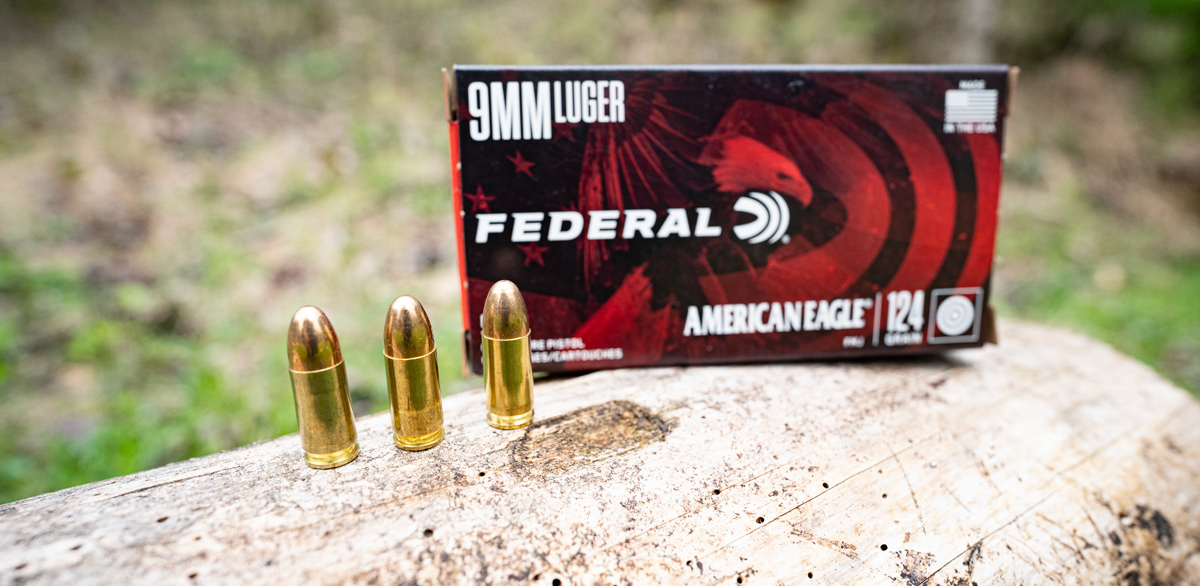 Federal American Eagle 9mm ammo box and loose rounds on a log at a shooting range