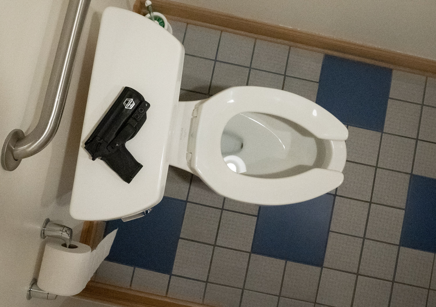 Pistol left on top of a toilet in a restroom.